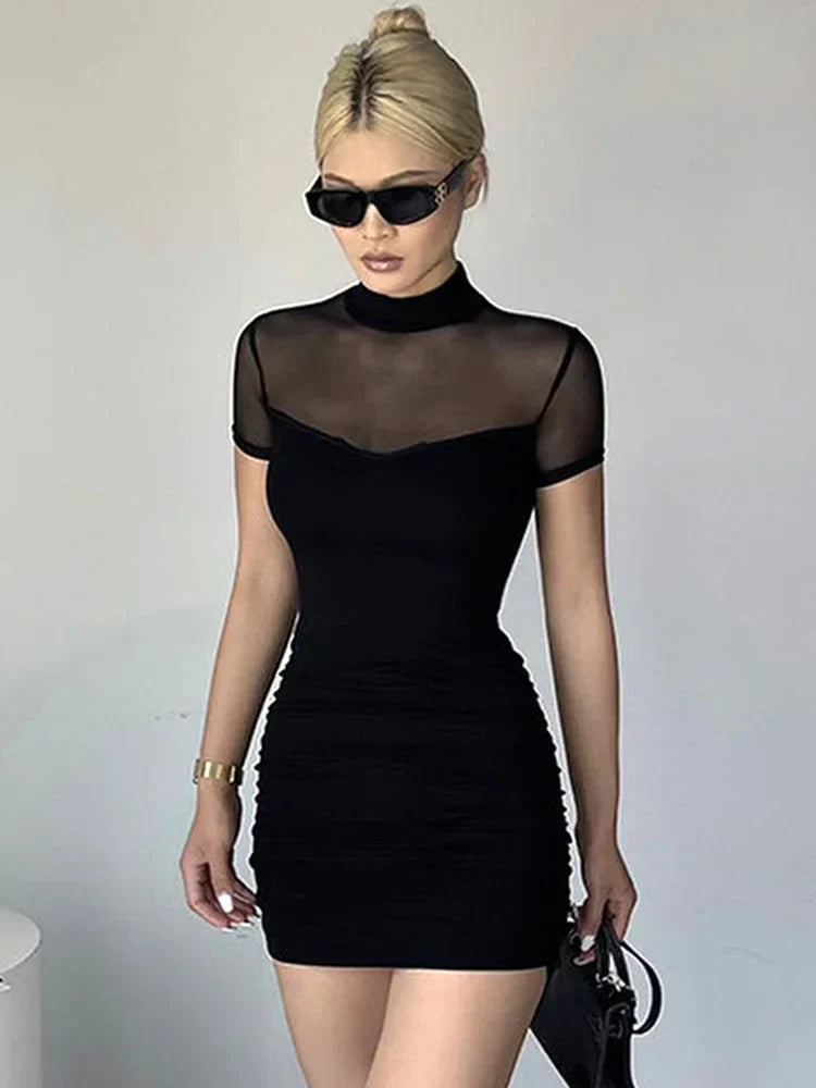 A woman in a black ruched mesh top dress with a mock neck, short sleeves, and sunglasses.