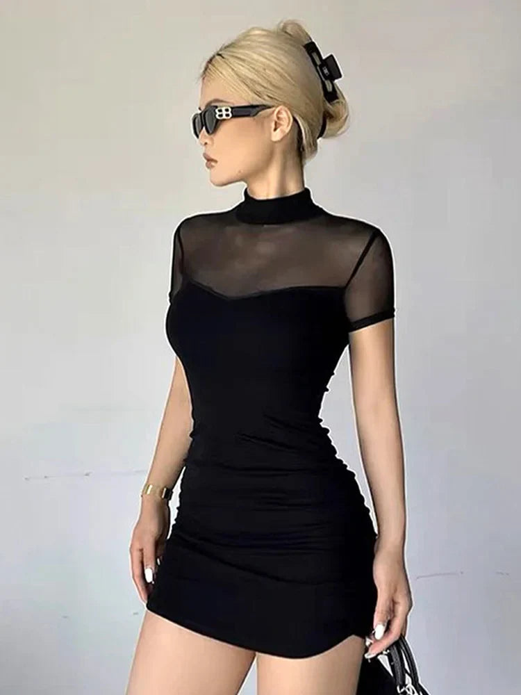 A woman in a black ruched mesh top dress with a mock neck, short sleeves, and sunglasses, shown from the side.