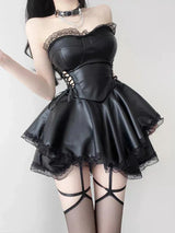 A woman wearing a black strapless leather-like dress with lace trim and garter straps, posing against a white wall.