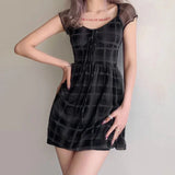 Woman wearing a short black and gray plaid dress with sheer short sleeves and a tie-front detail.