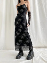 Full-body shot of a woman in a black floral slip dress, lace gloves, and platform boots.