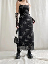A woman poses in a black floral slip dress, lace gloves, and platform boots, with a black shoulder bag.