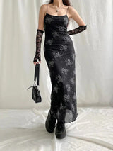 A woman wearing a long, black slip dress with a white floral print, black lace gloves, and black platform boots, holding a small black shoulder bag.