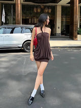 A woman in a brown halter dress and red purse stands on a street.