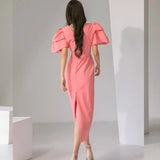 back view of a woman in a coral pink midi dress with dramatic puff sleeves and a slit hem