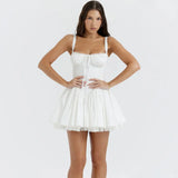 Woman posing with hands on hips wearing a white mini dress with spaghetti straps, a sweetheart neckline, and a pleated skirt with lace trim.