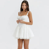 Woman wearing a white mini dress with spaghetti straps, a sweetheart neckline, and a pleated skirt with lace trim.