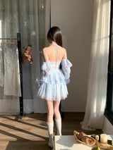 The back of a young woman in a light blue, ruffled, off-the-shoulder dress with lace trim, showing the tie-back detail.