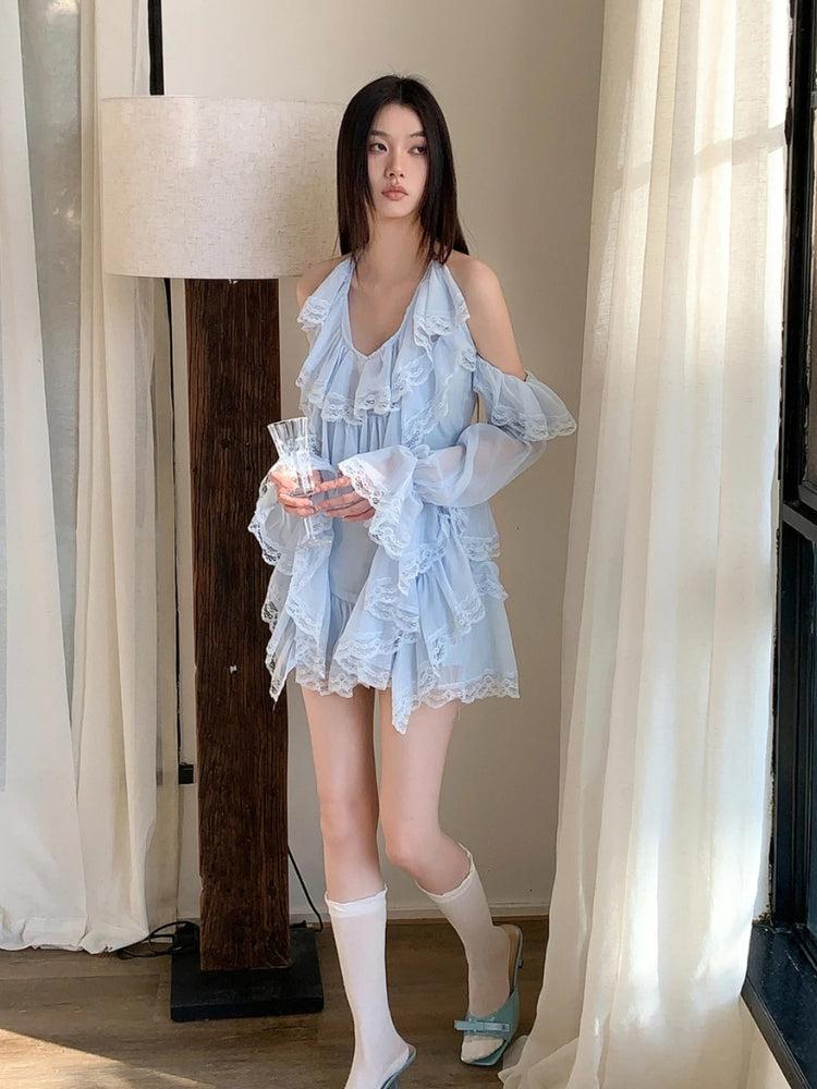 A young woman stands in a light blue, ruffled, off-the-shoulder dress with lace trim, holding a glass.