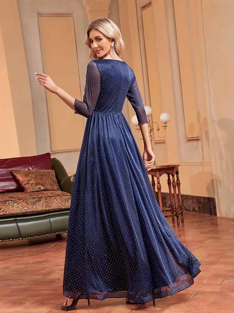 Rear view of a woman in a navy blue sparkly A-line evening gown with a plunging V-neck and sheer three-quarter sleeves, turning to the side.