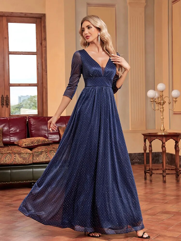 Woman in a navy blue sparkly A-line evening gown with a plunging V-neck and sheer three-quarter sleeves, looking over her shoulder.