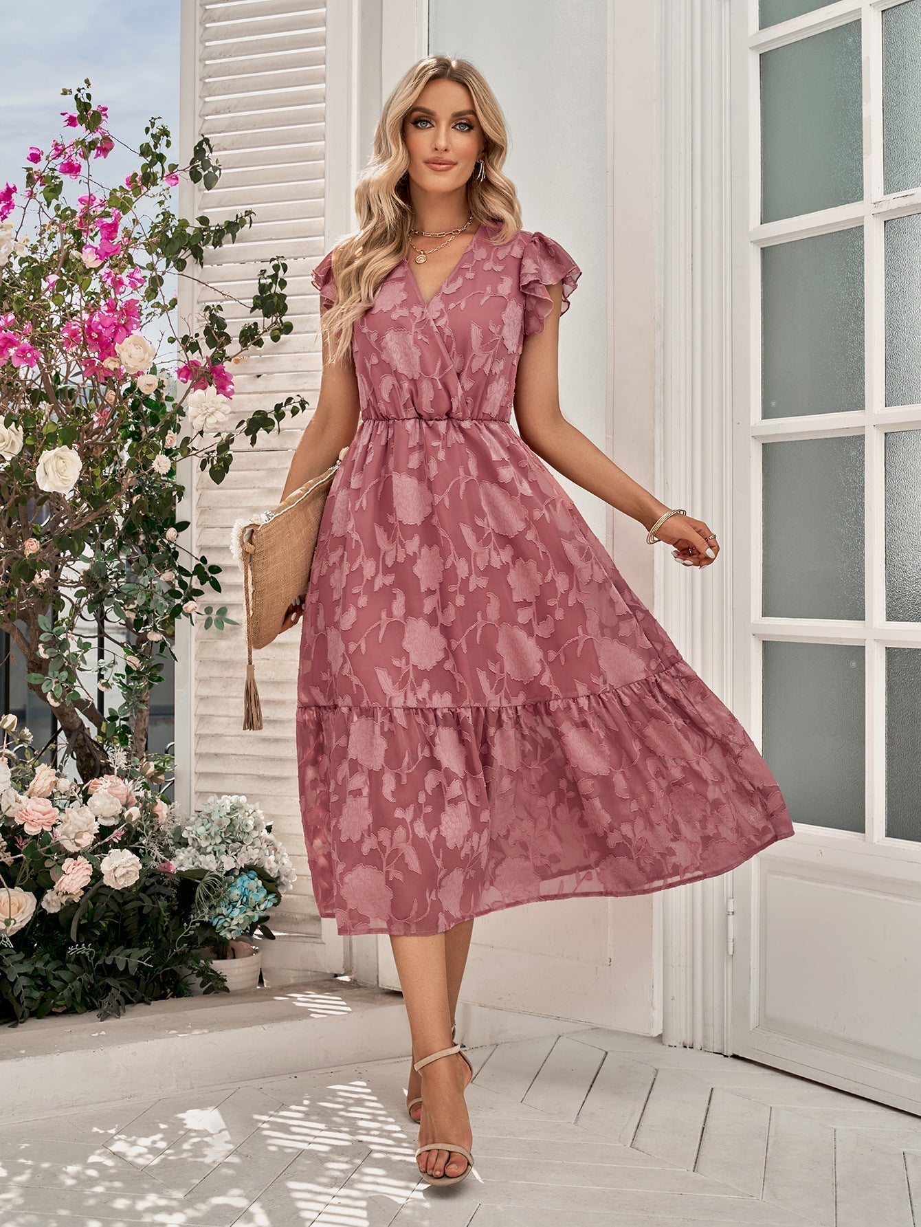 A woman models a pink floral print midi dress with ruffled sleeves and a tiered skirt.