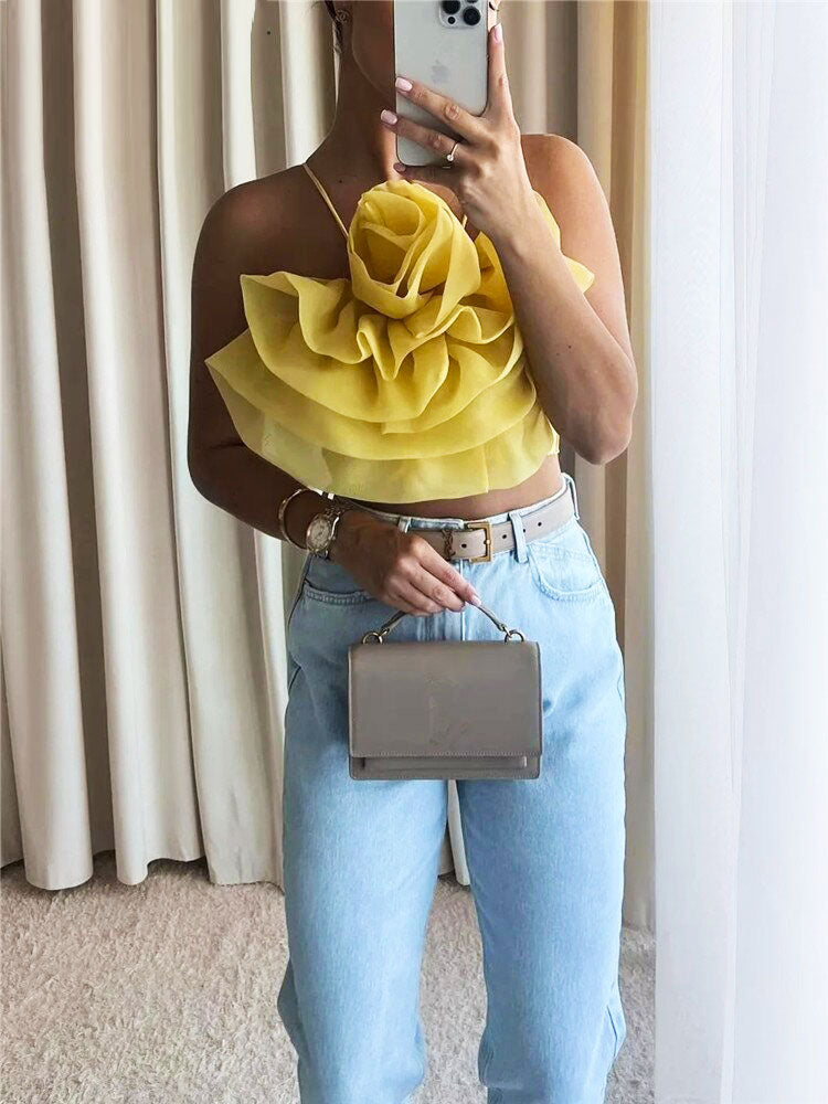 A woman holding a phone and a purse, wearing a yellow floral strapless top and light blue jeans.