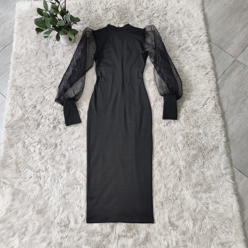 A black midi dress with sheer puff sleeves and a mock neck laid flat on a white fluffy rug.