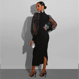 A woman from the side wearing a black midi dress with sheer puff sleeves and a mock neck, showing the back zipper and side slit.
