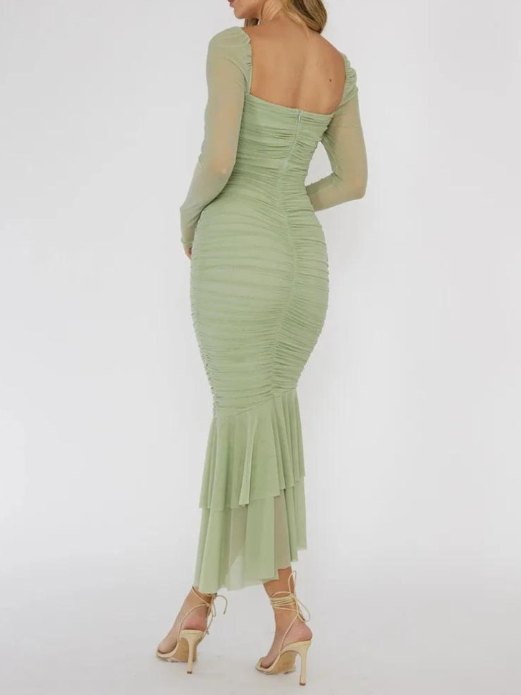 Back view of a woman in a green ruched midi dress with sheer long sleeves and a ruffled hem