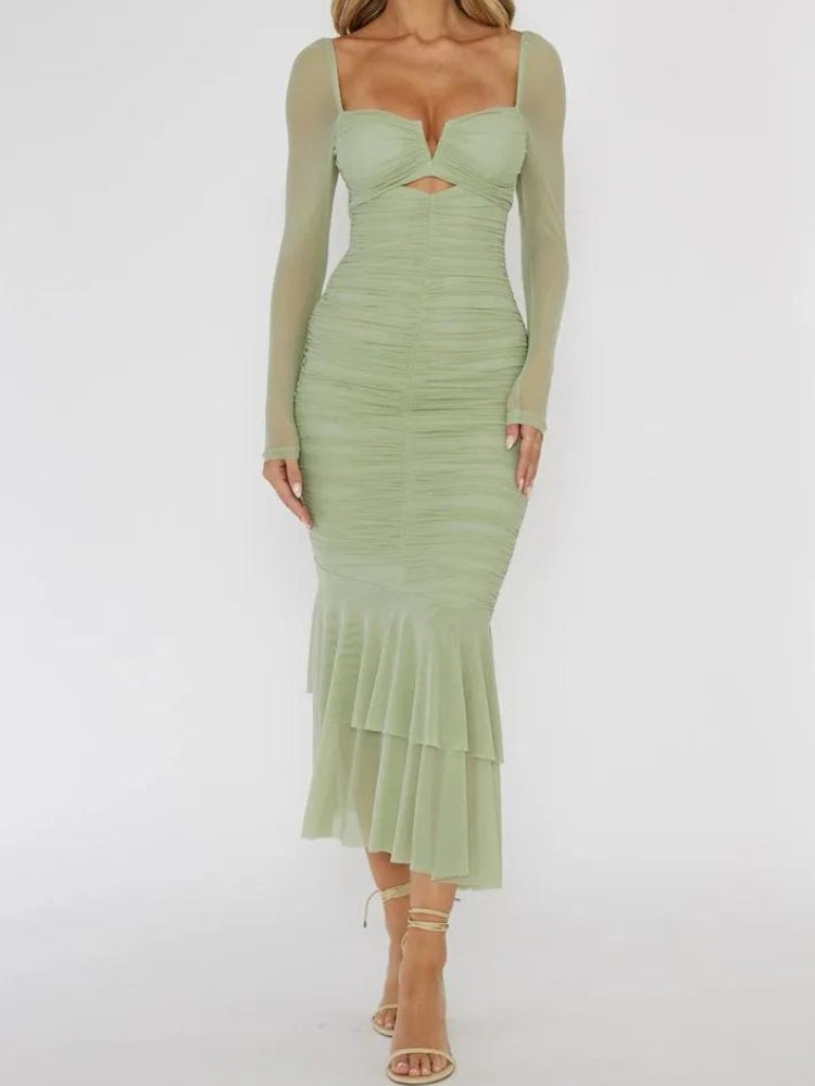 Front view of a woman in a green ruched midi dress with sheer long sleeves and a cutout detail