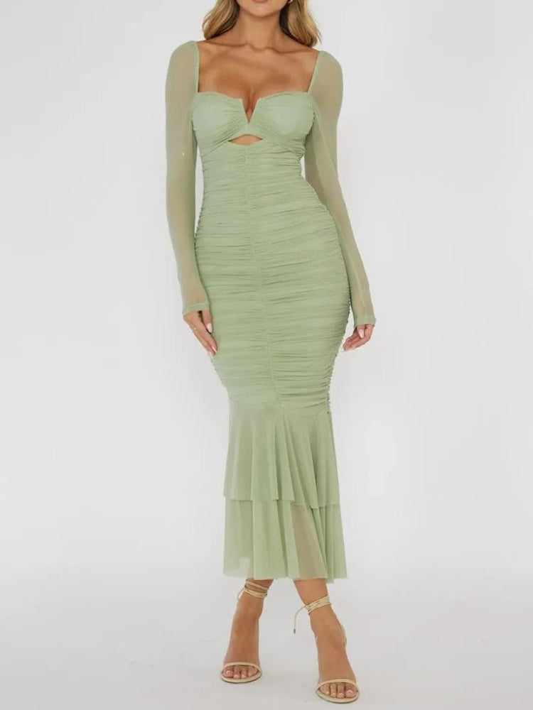 Woman wearing a green ruched midi dress with sheer long sleeves and a cutout detail