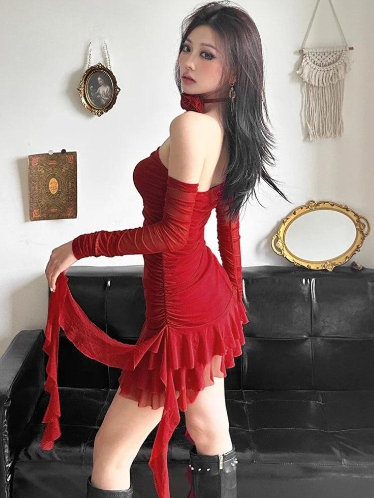 A woman in a red ruched mini dress with sheer sleeves and ruffles, posing sideways