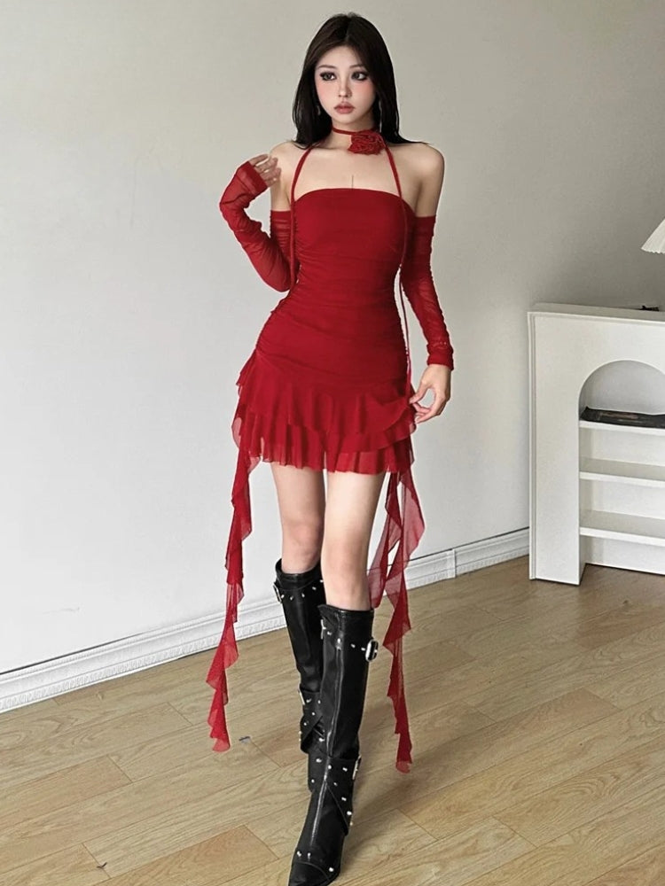 A full-body shot of a woman in a red ruched mini dress with sheer sleeves, ruffles, and black boots