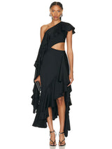 A woman in a black one-shoulder ruffled dress with a cut-out and high-low hem, holding a clutch.