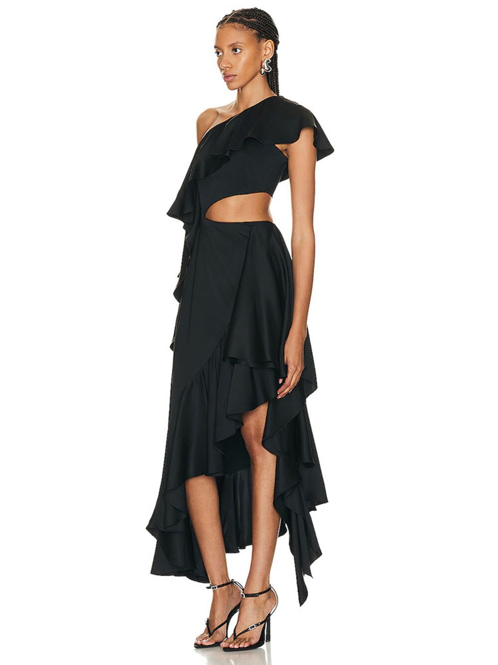 A woman in a black one-shoulder ruffled dress with a cut-out and high-low hem, shown from the side, holding a clutch.