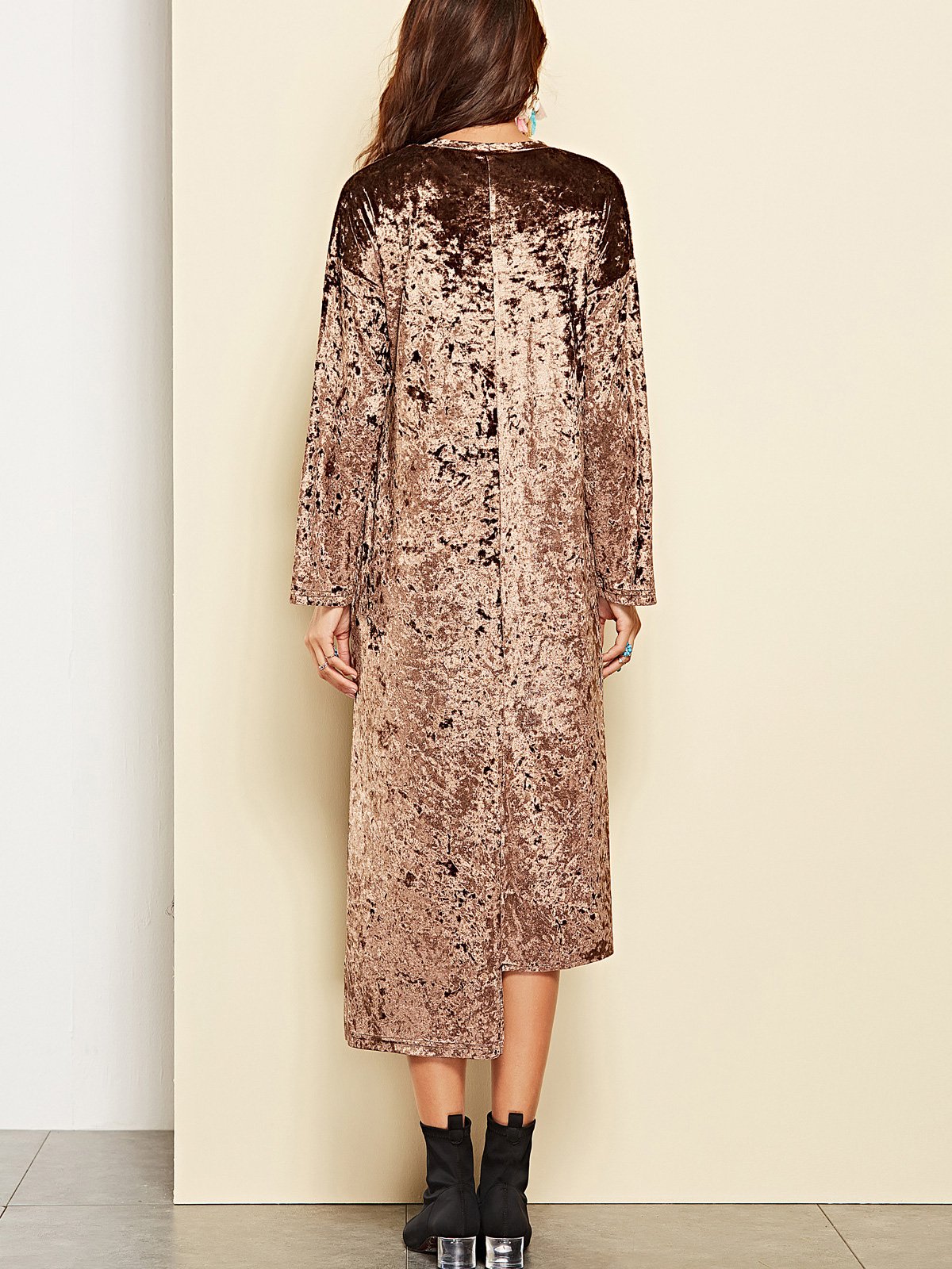 Back view of a woman wearing a crushed velvet brown dress with long sleeves and a high-low hemline, paired with black boots.