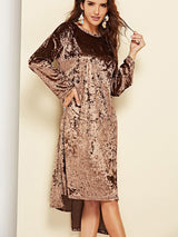 Front view of a woman posing in a crushed velvet brown dress, her hand on her hip, highlighting the dress's silhouette.