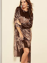 Woman wearing a crushed velvet brown dress with a high-low hemline and sheer underlay, accessorized with colorful earrings and rings.