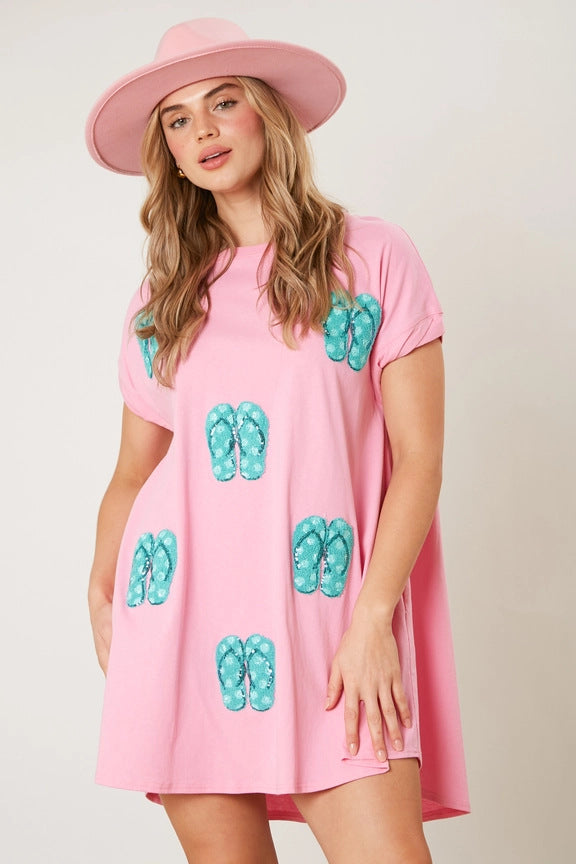 A woman wearing a pink t-shirt dress with sequined flip-flop prints and a pink hat.