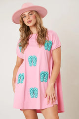 A woman wearing a pink t-shirt dress with sequined flip-flop prints and a pink hat.