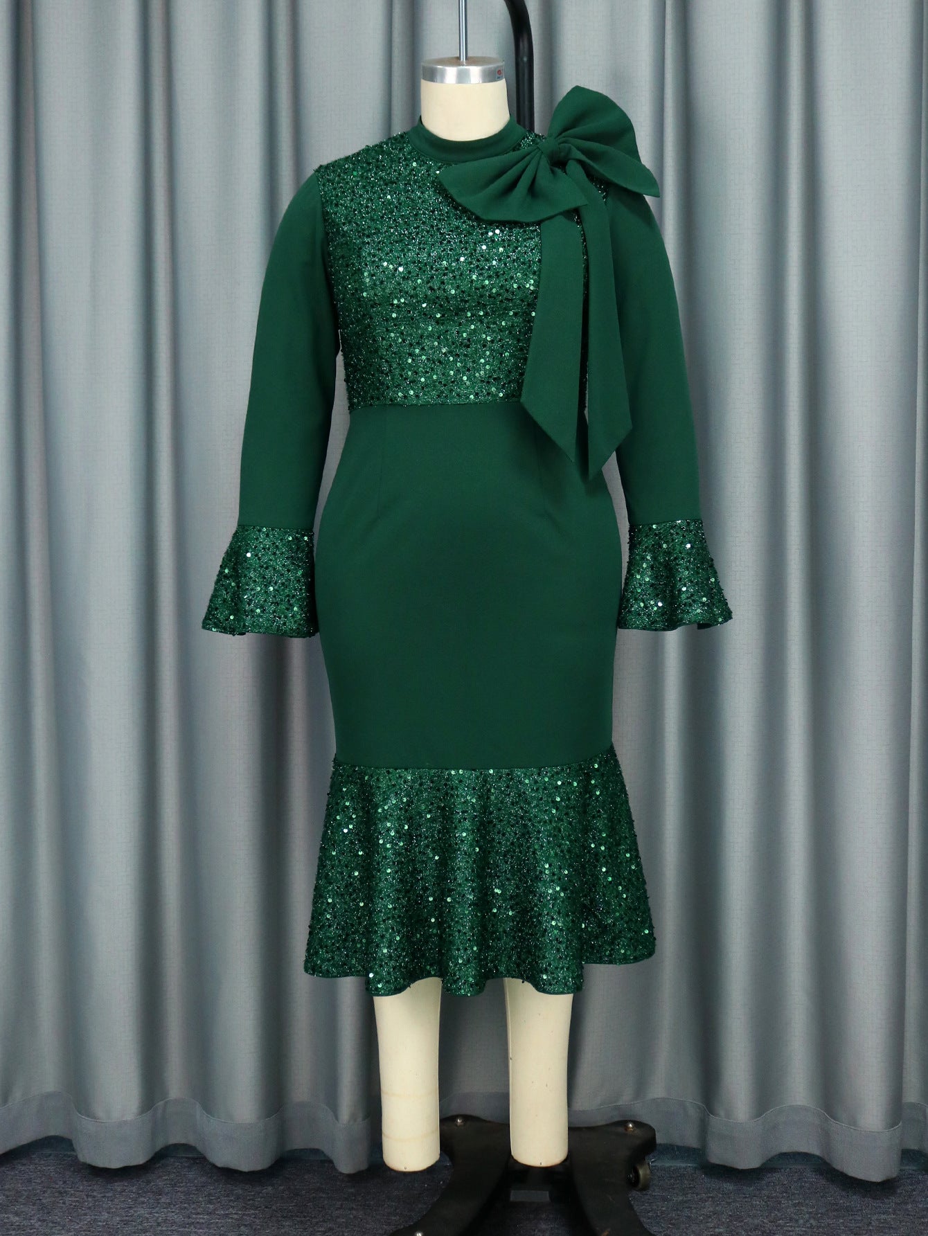 A green sequined dress with a bow detail displayed on a mannequin.