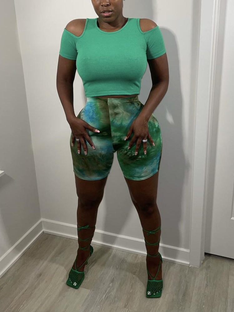 Woman wearing a green cropped ribbed t-shirt with cold shoulder cutouts and blue and green tie-dye shorts