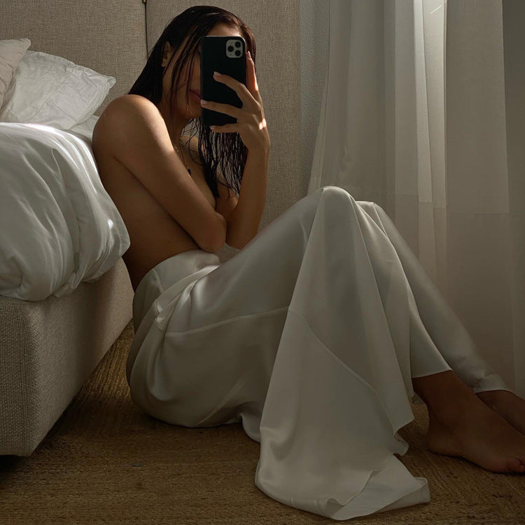 A woman sits on the floor in a bedroom wearing a white satin maxi skirt.