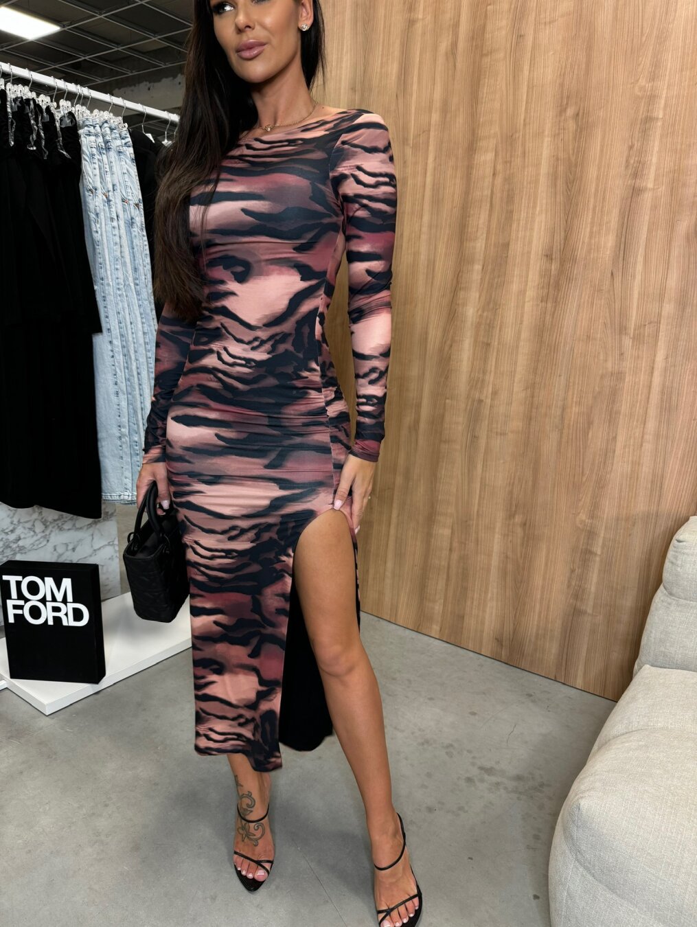 Woman in a long-sleeved tiger print dress with a high slit, wearing black strappy heels and holding a black handbag.
