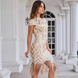 Woman in a beige and gold sequined short-sleeved dress with a fringe hem, posing in a colonnade.
