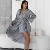 Woman in a grey satin robe and cami dress posing in a modern living room.