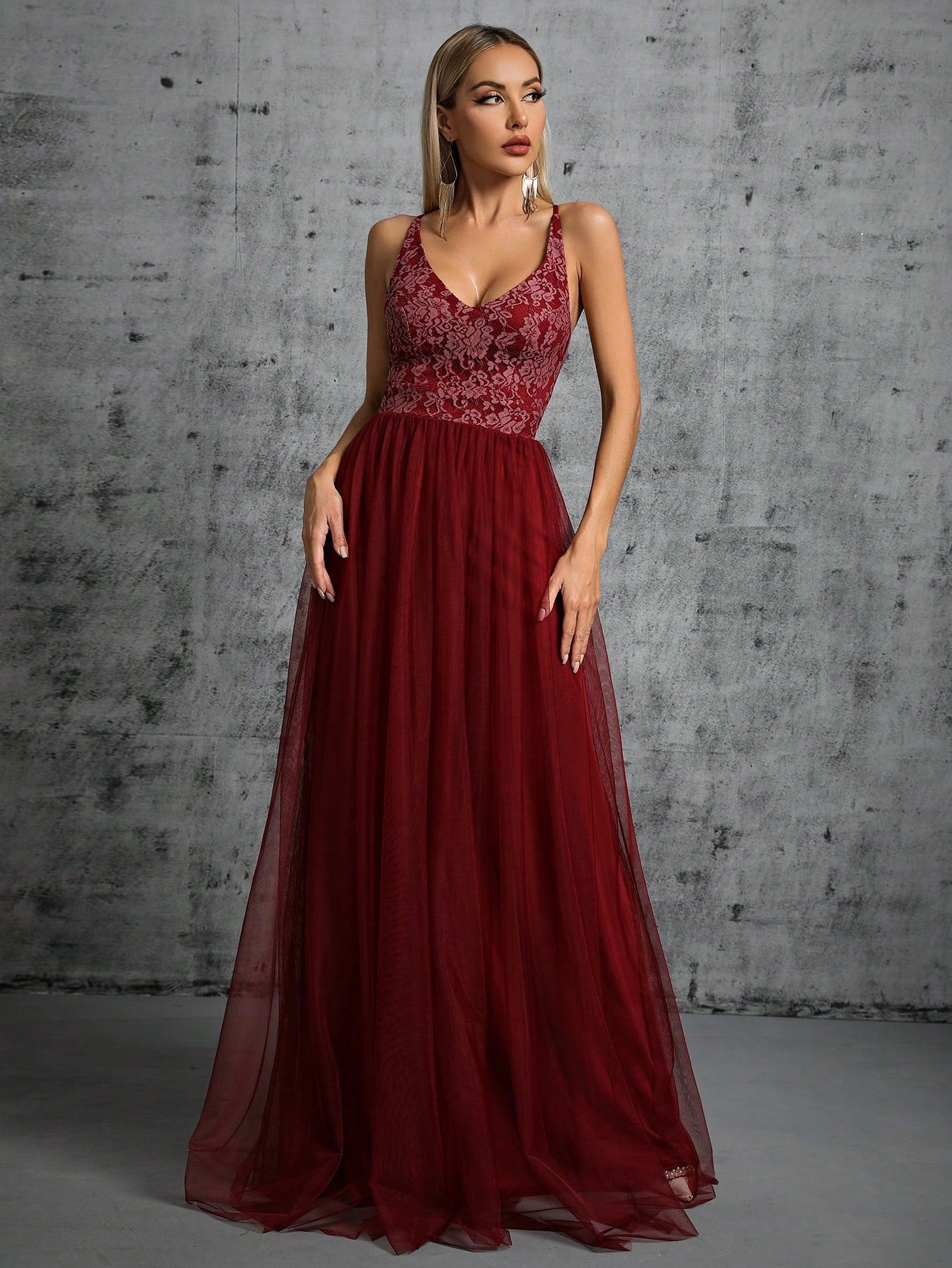 Full-length shot of a model wearing a dark red A-line gown with a V-neck and intricate lace detailing on the bodice.