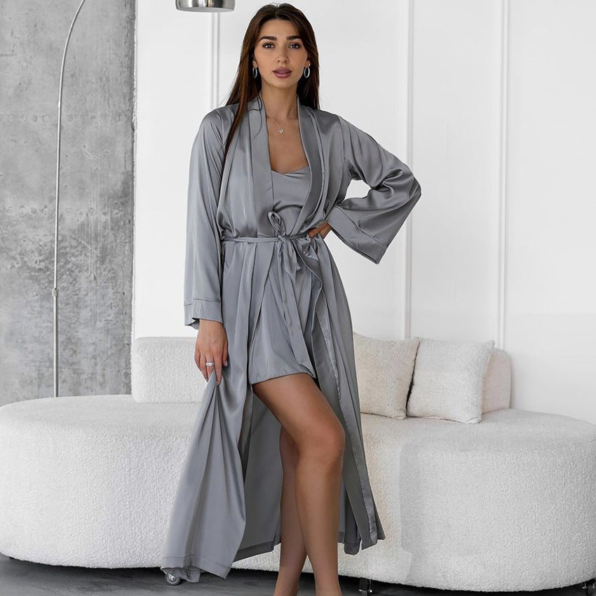 Woman in a grey satin robe and cami dress standing in a modern living room.