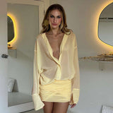 A woman wearing a pale yellow sheer ruched dress with a plunging neckline and long sleeves.