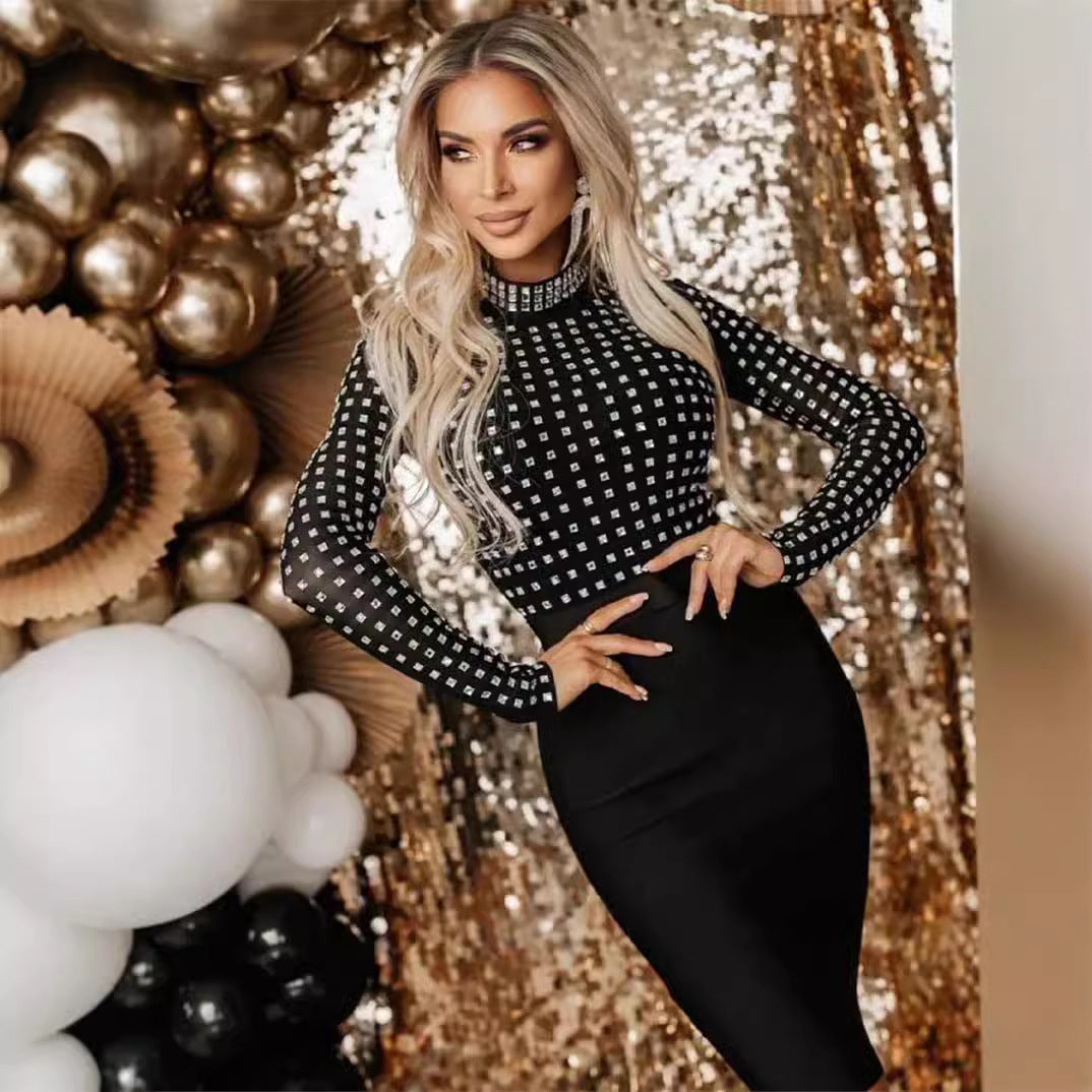 Blonde woman with hands on hips wearing a black long-sleeved mock neck dress with sheer rhinestone-embellished top and black pencil skirt, posing in front of a gold sequined backdrop with balloons.