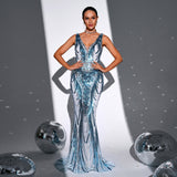 Woman in a white and blue sequined mermaid gown with a v-neck and sleeveless design, hands on hips.