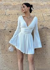Woman wearing a white mini dress with flared sleeves and a deep V-neck.