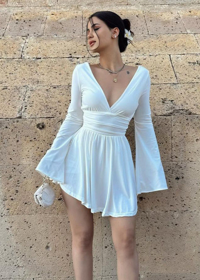 Woman wearing a white mini dress with flared sleeves and a deep V-neck.