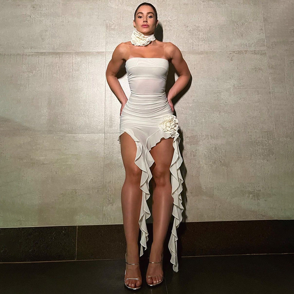 A woman stands with her hands on her hips in a white strapless dress with ruffled detailing.