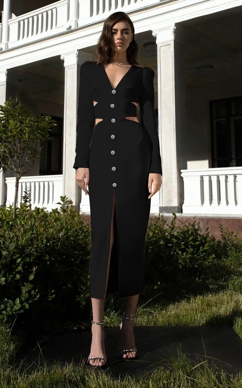 Woman wearing a black midi dress with cut-outs and a high slit, standing in a garden.