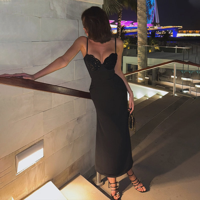 A woman in a black sequined midi dress leans against a railing on a staircase.