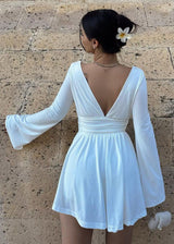 Back view of a woman in a white mini dress with flared sleeves and a deep V-neck.