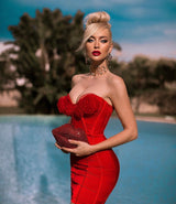 A woman in a red strapless dress with rose embellishments and a red sequined clutch, standing by a pool.