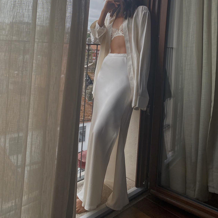 A woman stands on a balcony wearing a white satin maxi skirt and a matching shirt.